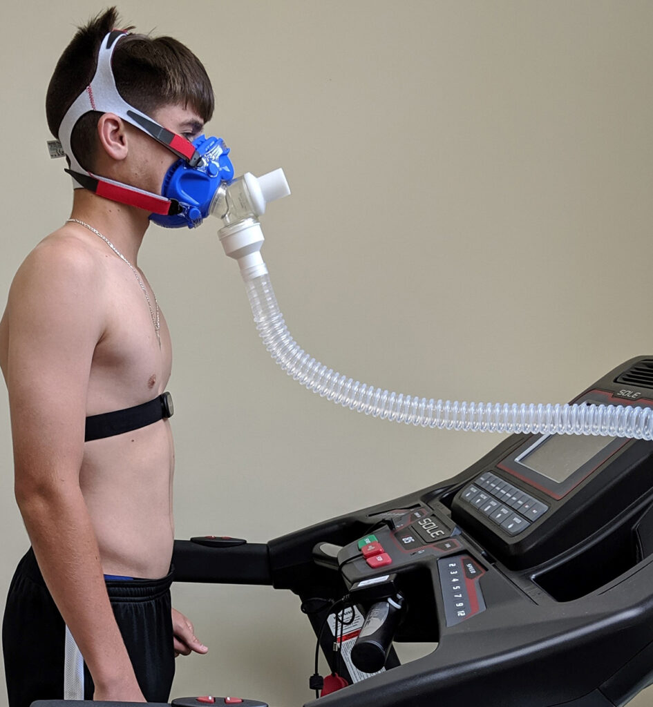 A young athlete standing on a treadmill wearing a face mask for maximal oxygen testing